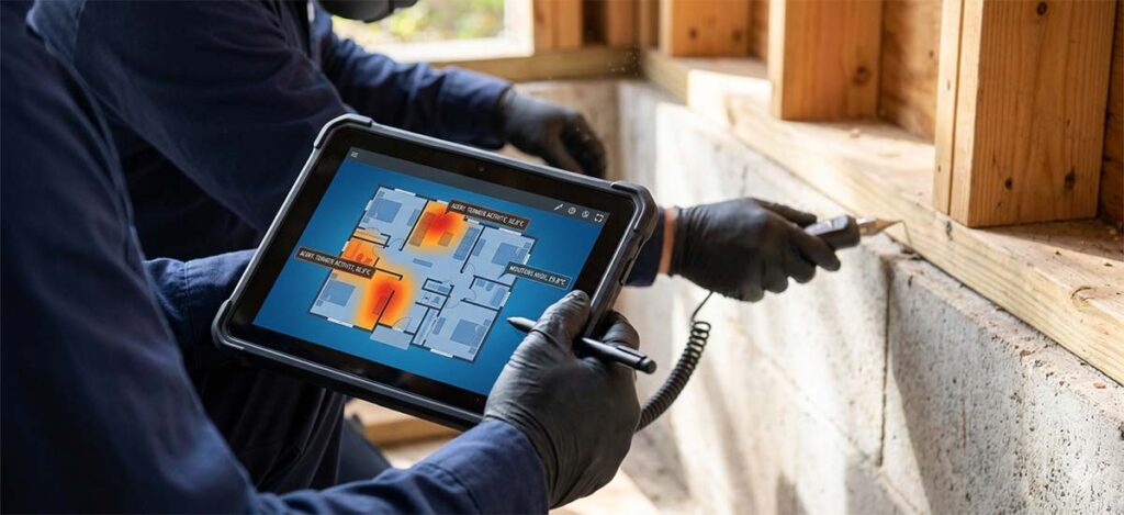 A pest control technician in protective clothing and gloves holding a thermal pest-detection device